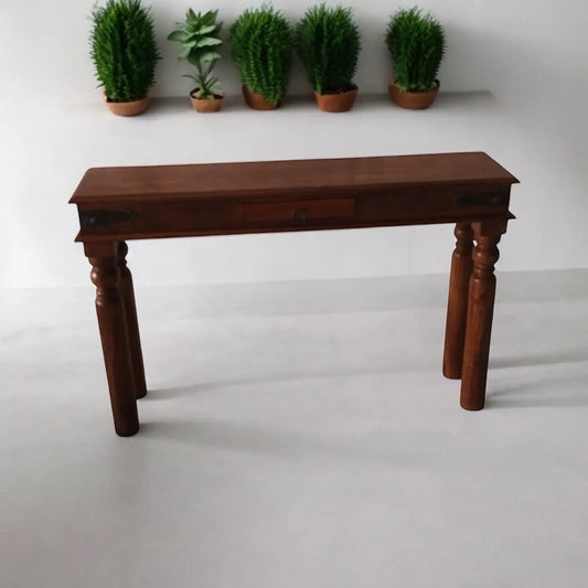 Solid wood console table with turned legs by Bert Joseph, against a white wall with potted plants.